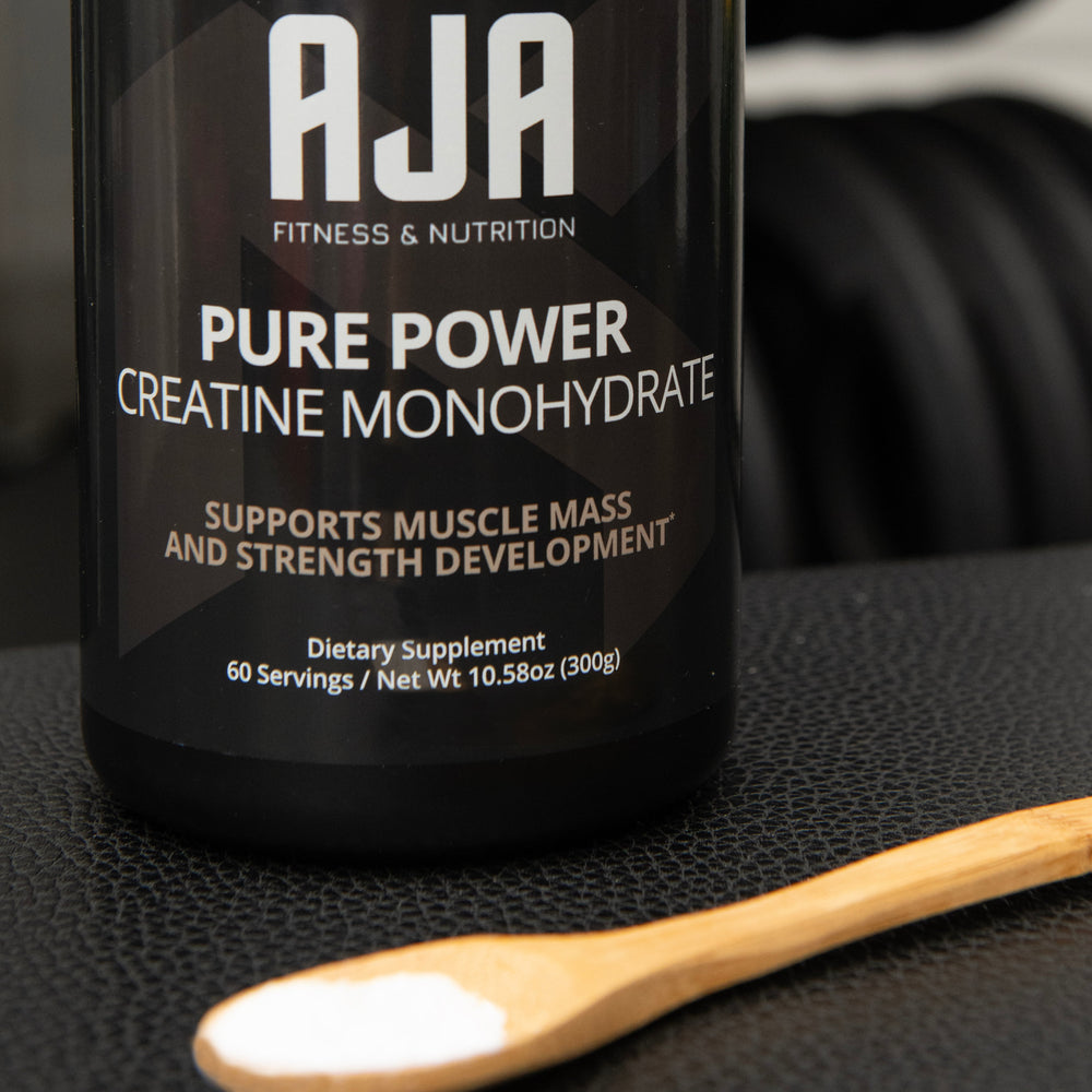 
                      
                        AJA Pure Power Creatine Monohydrate supplement container on a black surface with a wooden spoon.
                      
                    